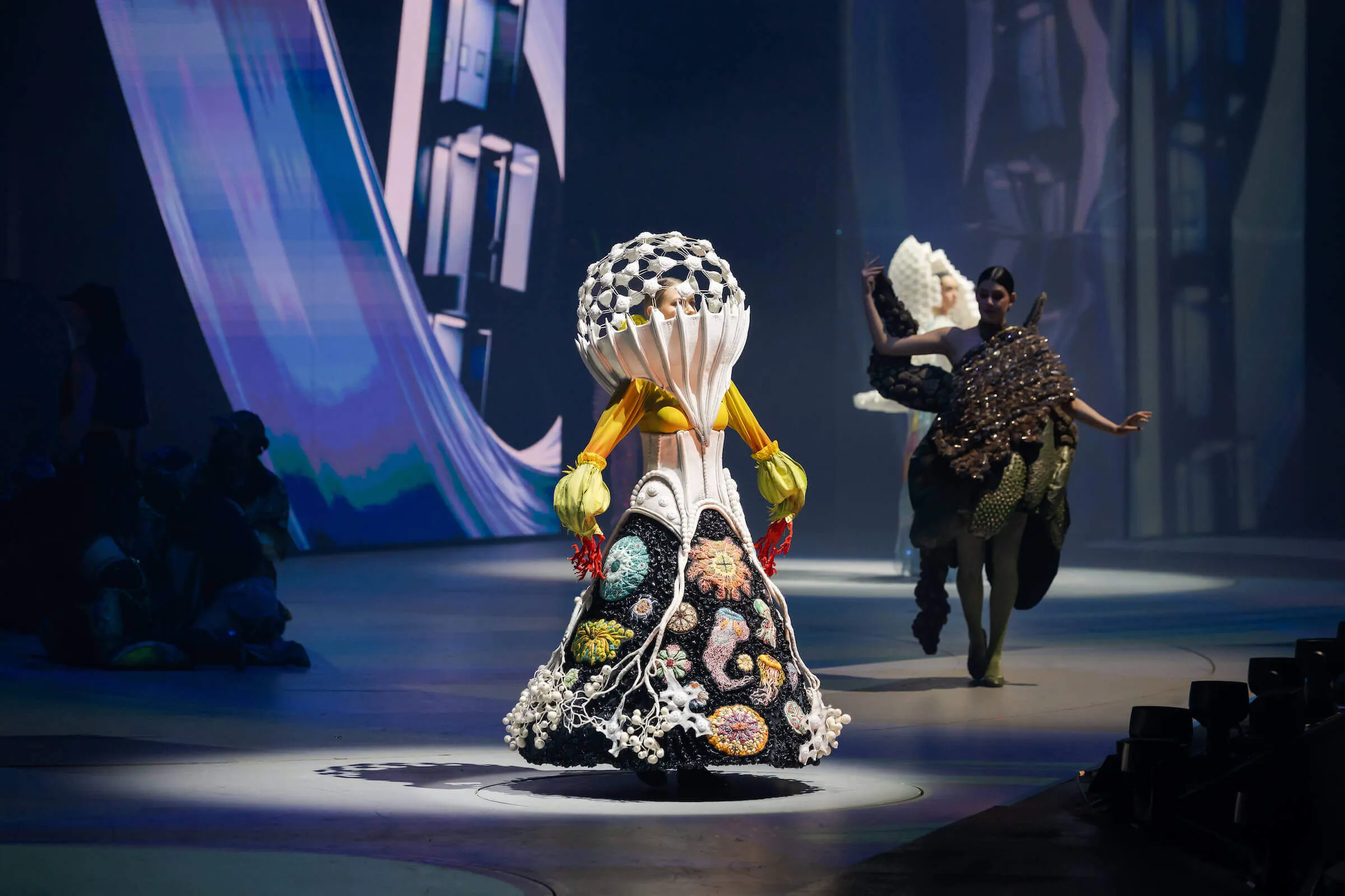 Models walking on runway wearing avant-garde floral and coral-inspired couture dresses with sculptural headpieces.